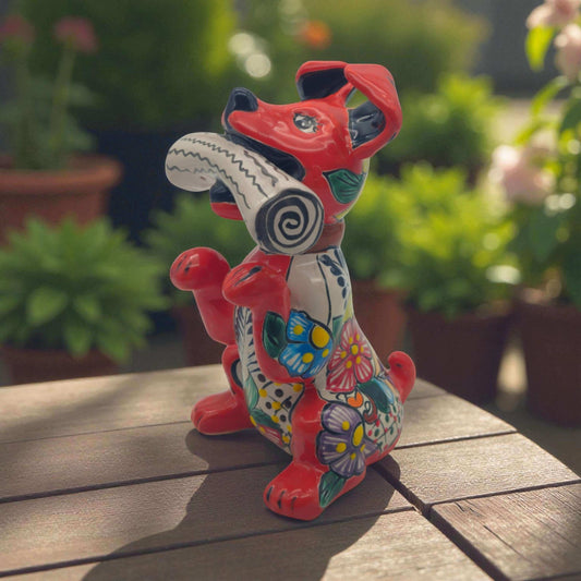 Talavera Dog Holding Newspaper Statue | Colorful Mexican Garden Art - hand-painted red Talavera dog with floral motifs holding a black-and-white newspaper
