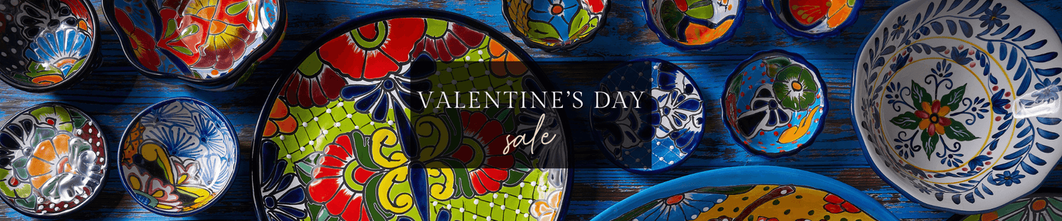 Colorful hand-painted ceramic plates and bowls arranged on a blue wooden table, perfect for a Valentine’s Day sale banner