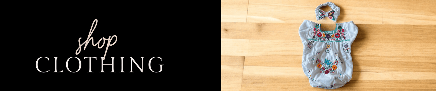 Baby girl embroidered romper and matching headband on wood surface beside 'shop clothing' sign