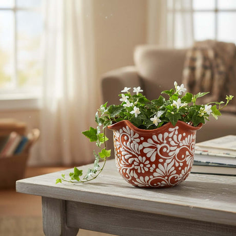 The Talavera Hub brown and white ceramic planter with wavy rim, hand-painted floral motifs, holding a plant with white flowers.