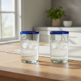 The Talavera Hub hand-blown clear glass tumblers with cobalt blue rims, 5" tall, sold as a set of two.