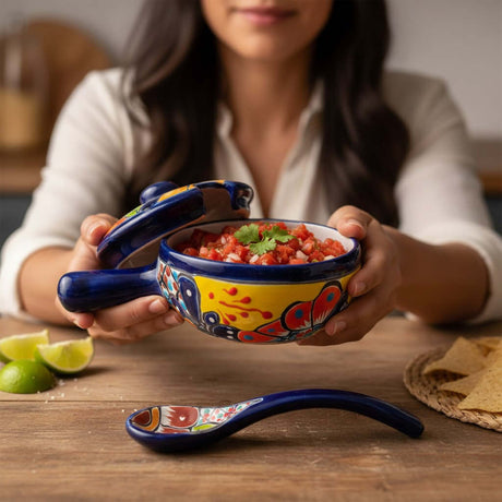 The Talavera Hub hand-painted ceramic salsa bowl with lid and spoon, featuring multicolor floral and geometric patterns on a yellow and blue base.