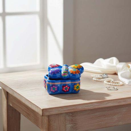 The Talavera Hub hand-painted blue ceramic butterfly jewelry box with floral patterns on a wooden table.