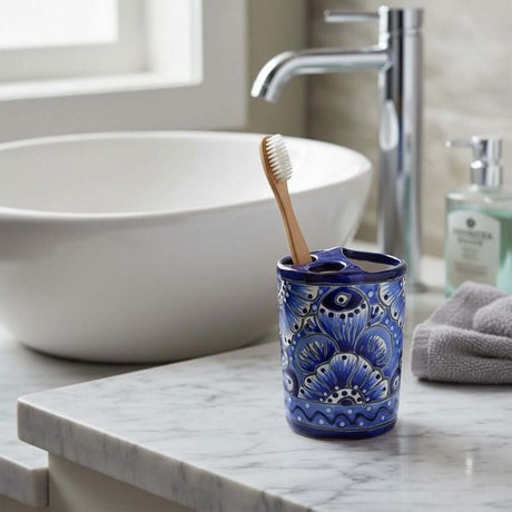 The Talavera Hub hand-painted blue and white ceramic toothbrush holder with floral motifs on a marble bathroom vanity.
