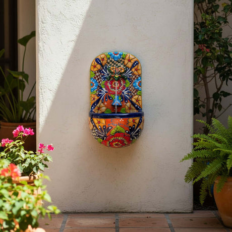The Talavera Hub handcrafted ceramic wall fountain with frog spout, featuring vibrant floral and geometric patterns in orange, blue, red, yellow, and green.