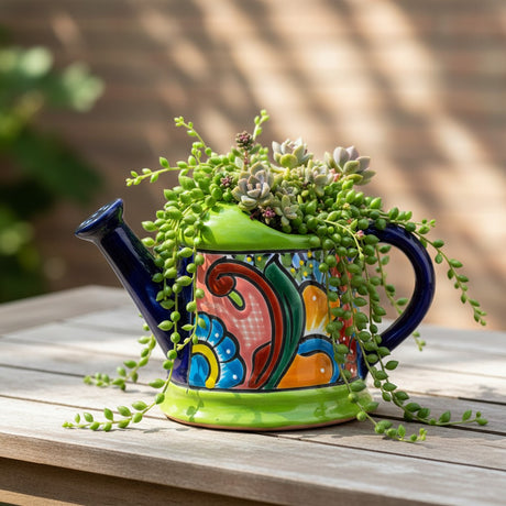 The Talavera Hub hand-painted ceramic watering can planter with blue spout, green base, and vibrant floral designs.