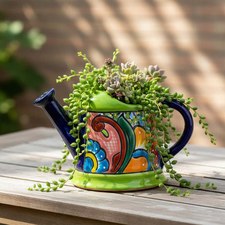 The Talavera Hub hand-painted ceramic watering can planter with blue spout, green base, and vibrant floral designs.