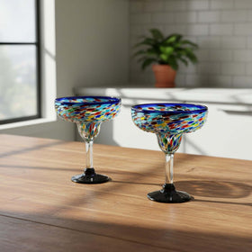 The Talavera Hub Mexican hand-blown margarita glasses with blue confetti rock design. Clear glass with colorful flecks and dark bases.