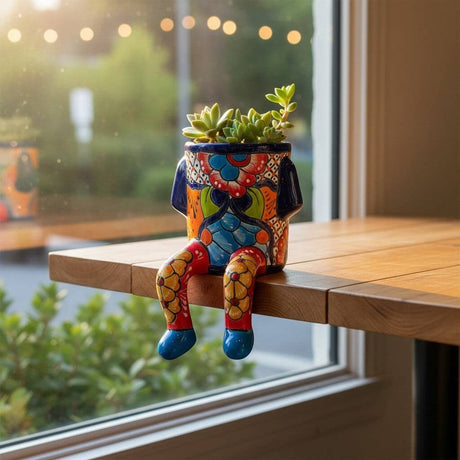 The Talavera Hub hand-painted ceramic planter with arms and legs, featuring colorful floral designs and blue feet.