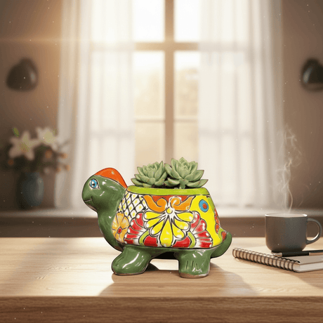 The Talavera Hub hand-painted green ceramic turtle planter with colorful floral designs and orange head, holding succulents.