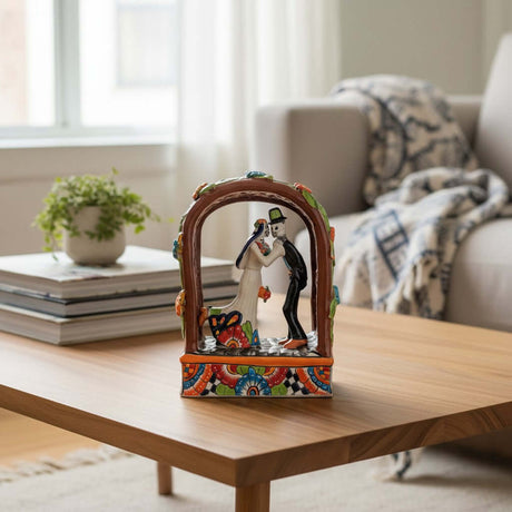 The Talavera Hub Day of the Dead wedding figurines, hand-painted ceramic bride and groom skeleton couple kissing under an arch.
