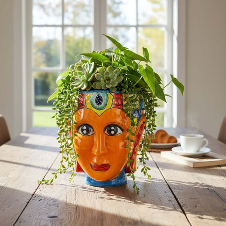The Talavera Hub hand-painted Talavera face planter, orange ceramic with colorful headdress and blue base.