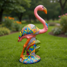 Colorful flamingo statue on grass with blurred greenery in the background