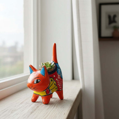 The Talavera Hub orange ceramic cat planter with multicolor floral motifs and blue ears, holding a succulent.