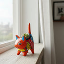 The Talavera Hub orange ceramic cat planter with multicolor floral motifs and blue ears, holding a succulent.