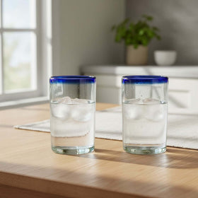 The Talavera Hub hand-blown clear glass tumblers with cobalt blue rims, 5" tall, sold as a set of two.