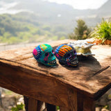Hand-Painted Guerrero Skull | Colorful Mexican Artisan Statue - two vibrant hand-painted Guerrero skulls on rustic wood table, Mexican pottery decor