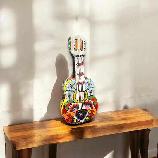 Talavera Guitar Statue | Hand-Painted Mexican Folk Art Decor - hand-painted colorful Talavera guitar statue with floral and geometric patterns on wooden bench
