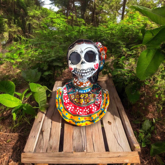 Vibrant Talavera Skeleton Woman Statue | Handcrafted Day of the Dead Decor on wooden pallet surrounded by greenery, hand-painted Mexican Talavera bust