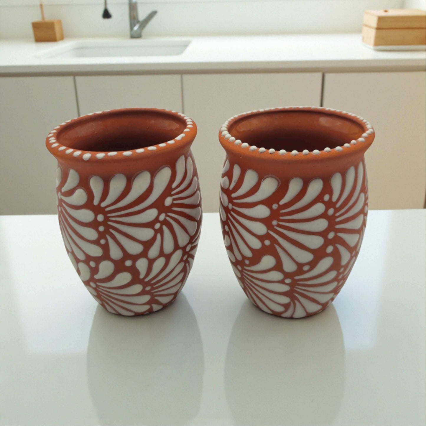 Terracotta Relief Cantarito | Handcrafted Mexican Pottery Cup with white raised floral relief, pair of handcrafted terracotta cantaritos on kitchen counter