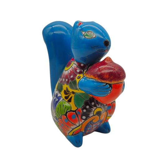 Blue Talavera squirrel statue holding a colorful nut on a white background