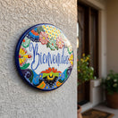 The Talavera Hub hand-painted ceramic Bienvenidos plaque with floral border in blue, orange, green, yellow, and red.