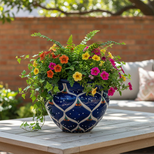 The Talavera Hub hand-painted ceramic pot in cobalt blue with peacock feather motifs in green, orange, and white. Features twin handles.