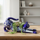 The Talavera Hub hand-painted blue Talavera cat planter with white floral accents, in a stretching pose.