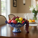 The Talavera Hub blue and white hand-painted ceramic fruit bowl filled with pomegranates, apples, lemons, strawberries, and grapes.