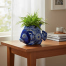 The Talavera Hub handcrafted blue and white ceramic fish planter with intricate floral patterns holding a green fern.