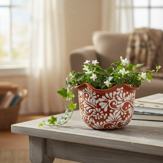 The Talavera Hub brown and white ceramic planter with wavy rim, hand-painted floral motifs, holding a plant with white flowers.