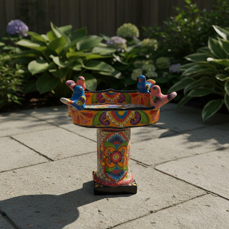 The Talavera Hub hand-painted ceramic bird bath with vibrant floral patterns and perched birds on a stone patio
