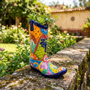The Talavera Hub hand-painted ceramic cowboy boot planter with vibrant floral patterns in a sunny garden setting.