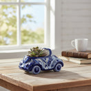 The Talavera Hub handmade blue and white ceramic car planter with floral motifs holding a small succulent on a desk.