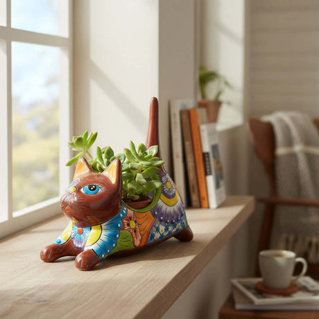 The Talavera Hub handmade ceramic cat planter with colorful floral patterns, holding a succulent on a wooden windowsill.