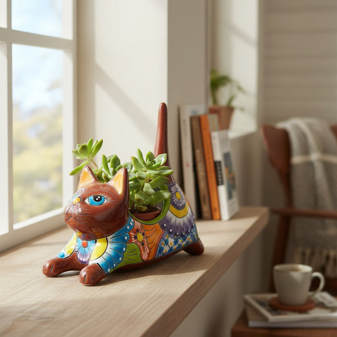 The Talavera Hub handmade ceramic cat planter with colorful floral patterns, holding a succulent on a wooden windowsill.