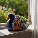 The Talavera Hub handmade Mexican ceramic duck planter with vibrant floral patterns and potted succulents on a windowsill