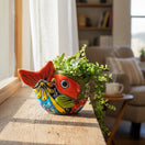 The Talavera Hub hand-painted ceramic fish planter in vibrant red, yellow, and blue with succulents on a windowsill.