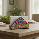The Talavera Hub hand-painted ceramic napkin holder with vibrant floral patterns on a wooden dining table.