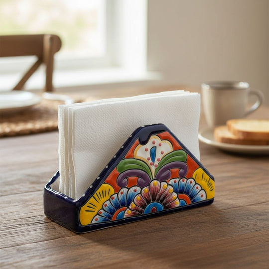 The Talavera Hub hand-painted ceramic napkin holder with vibrant floral patterns and a cobalt blue rim on a wood table.