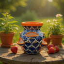 The Talavera Hub hand-painted ceramic strawberry planter with blue peacock pattern and orange rim on a wooden table.