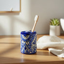 The Talavera Hub hand-painted ceramic toothbrush holder with blue and white floral motifs on a wooden bathroom vanity.