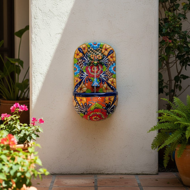 The Talavera Hub handcrafted ceramic wall fountain with frog spout, featuring vibrant floral and geometric patterns in orange, blue, red, yellow, and green.