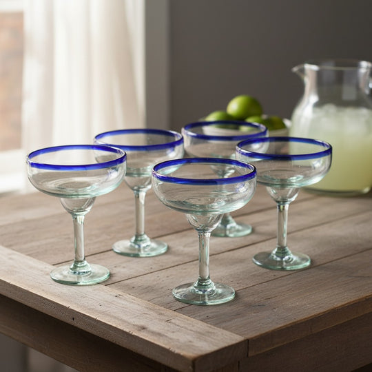 The Talavera Hub hand-blown Mexican margarita glasses with cobalt blue rims and clear, green-tinted recycled glass bodies.