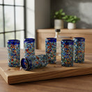 The Talavera Hub hand-blown glass double shot glasses with multicolor confetti accents and blue rims.