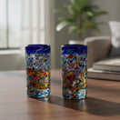 The Talavera Hub hand-blown glass double shot glasses with multicolor confetti accents and blue rims.