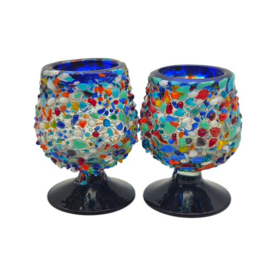 The Talavera Hub two confetti rock shot glasses with blue rims and pedestal bases, made of lead-free glass.