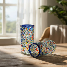 The Talavera Hub hand-blown glass tumbler with confetti pattern and blue rim. Clear glass with colorful chips and pebbled texture.