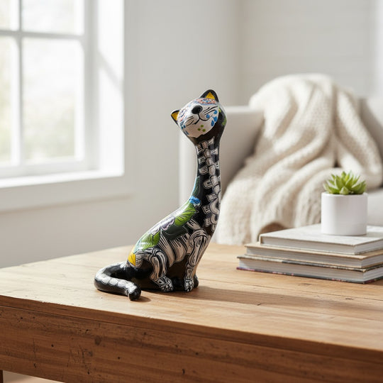 The Talavera Hub hand-painted ceramic cat figurine in Day of the Dead style, featuring floral motifs and skeletal details in orange, blue, and green.
