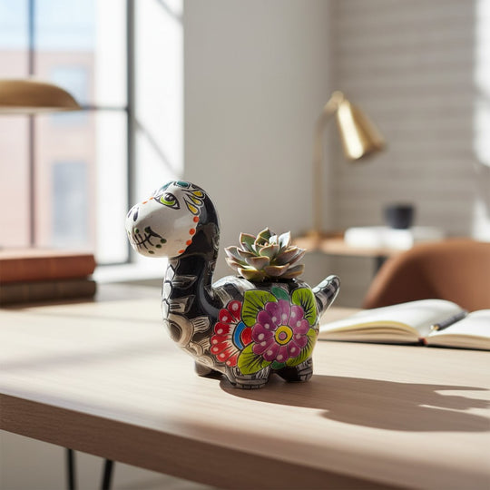 The Talavera Hub black ceramic brachiosaurus planter with Day of the Dead skull face and floral motifs in vibrant colors.